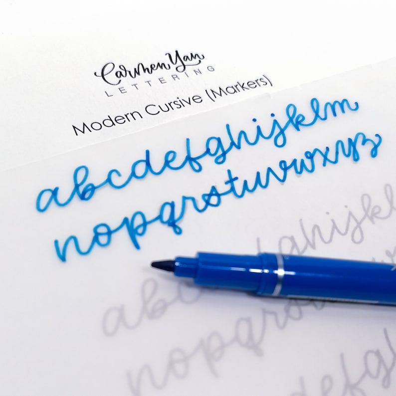 May include: A blue marker pen on a white surface with a blue cursive alphabet written on it. The text "CarWhen Yan LETTERING Modern Cursive (Markers)" is written at the top of the page.