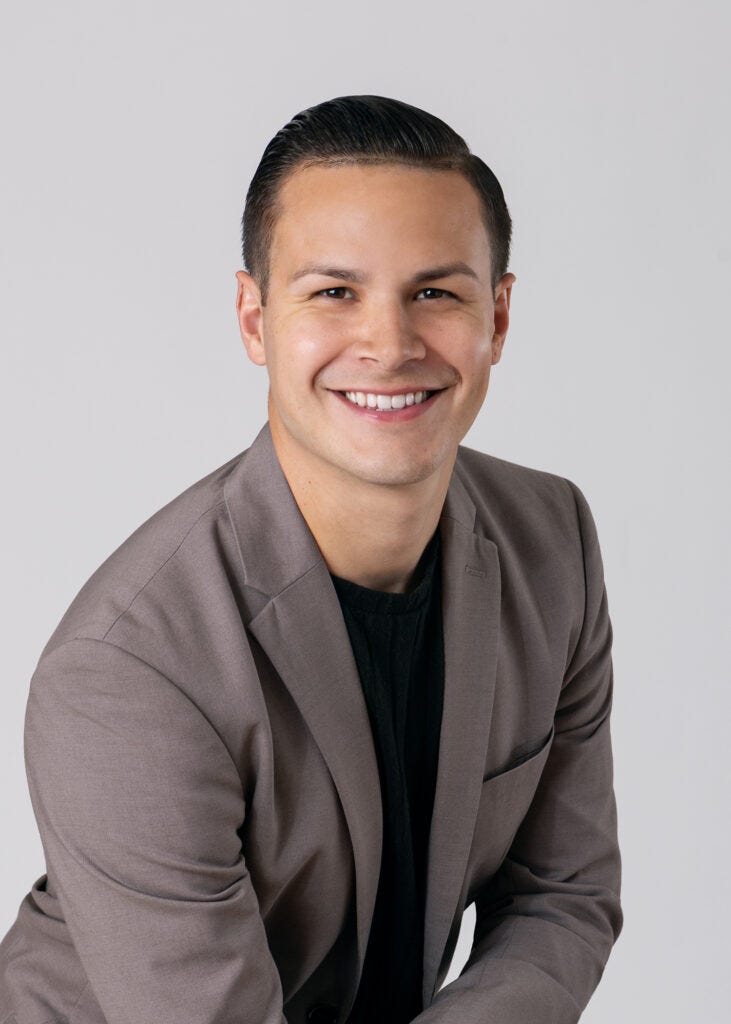 Carlos Foster wearing a gray blazer and black shirt, smiling