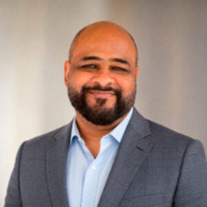 Homem negro de barba e terno cinza, camisa azul, sorri para a foto. Homem negro de barba e terno cinza, camisa azul, sorri para a foto.