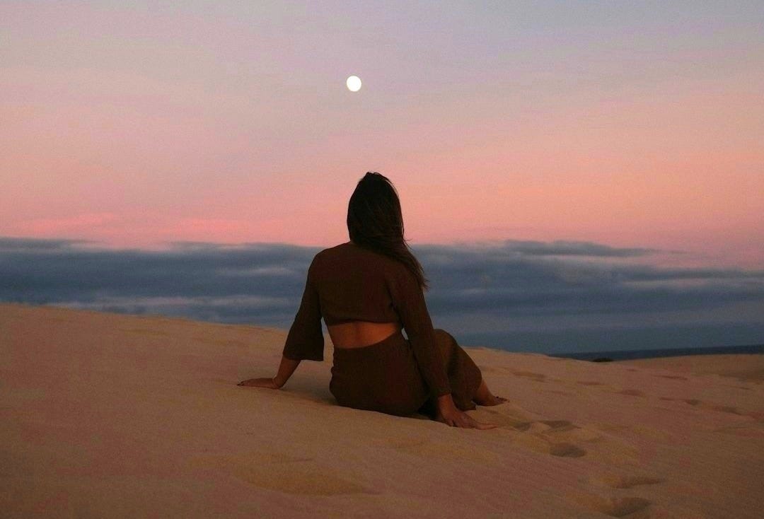 a woman sitting on top of a sandy beach