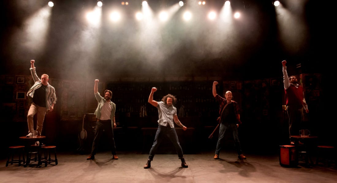 A group of men on stage with their fists in the air, with lights above them A group of men on stage with their fists in the air, with lights above them