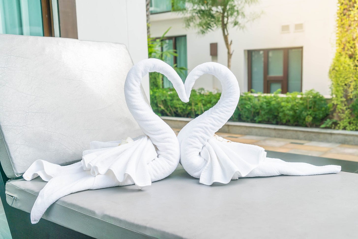 Image from Freepik; two white hotel towels folded into a pair of swans with their towelly beaks touching