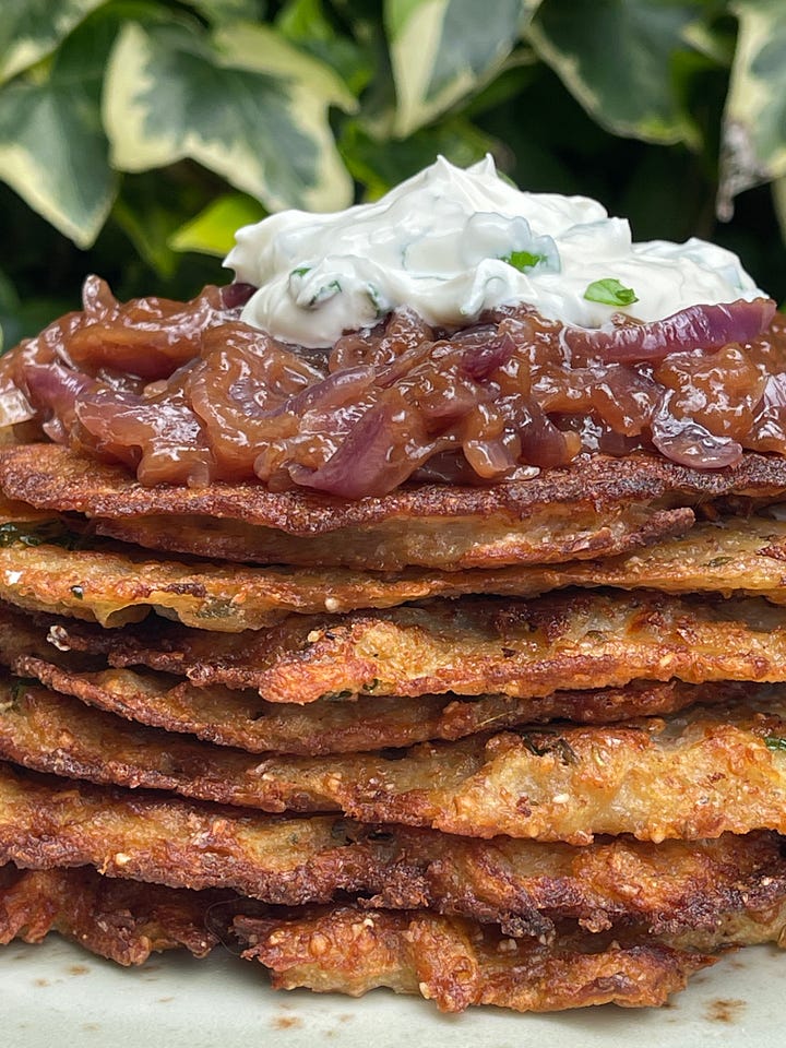 An overhead mise en place for bramboráky: grated potatoes, sliced red onions, whole wheat flour, a cracked egg, fresh parsley, dried marjoram, garlic paste, plant-based milk, sour cream, salt, and a glass of Czech beer.