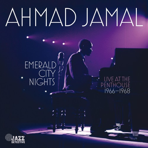 Young African American man named Ahmad Jamal, seated at a piano on a stage in a large, darkened room.