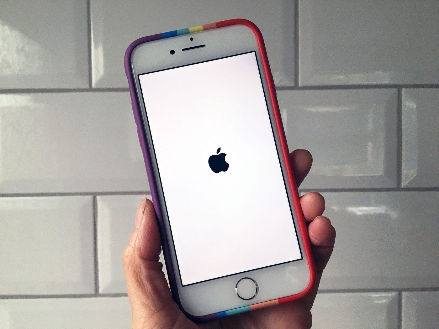 A hand holding an iPhone. The screen is showing the Apple icon of never-loading-again hell