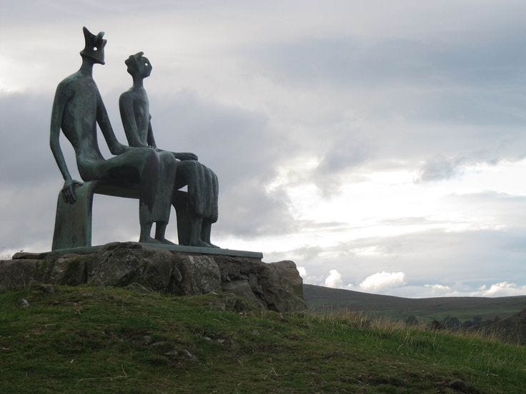 This may contain: two statues sitting on top of a lush green hillside