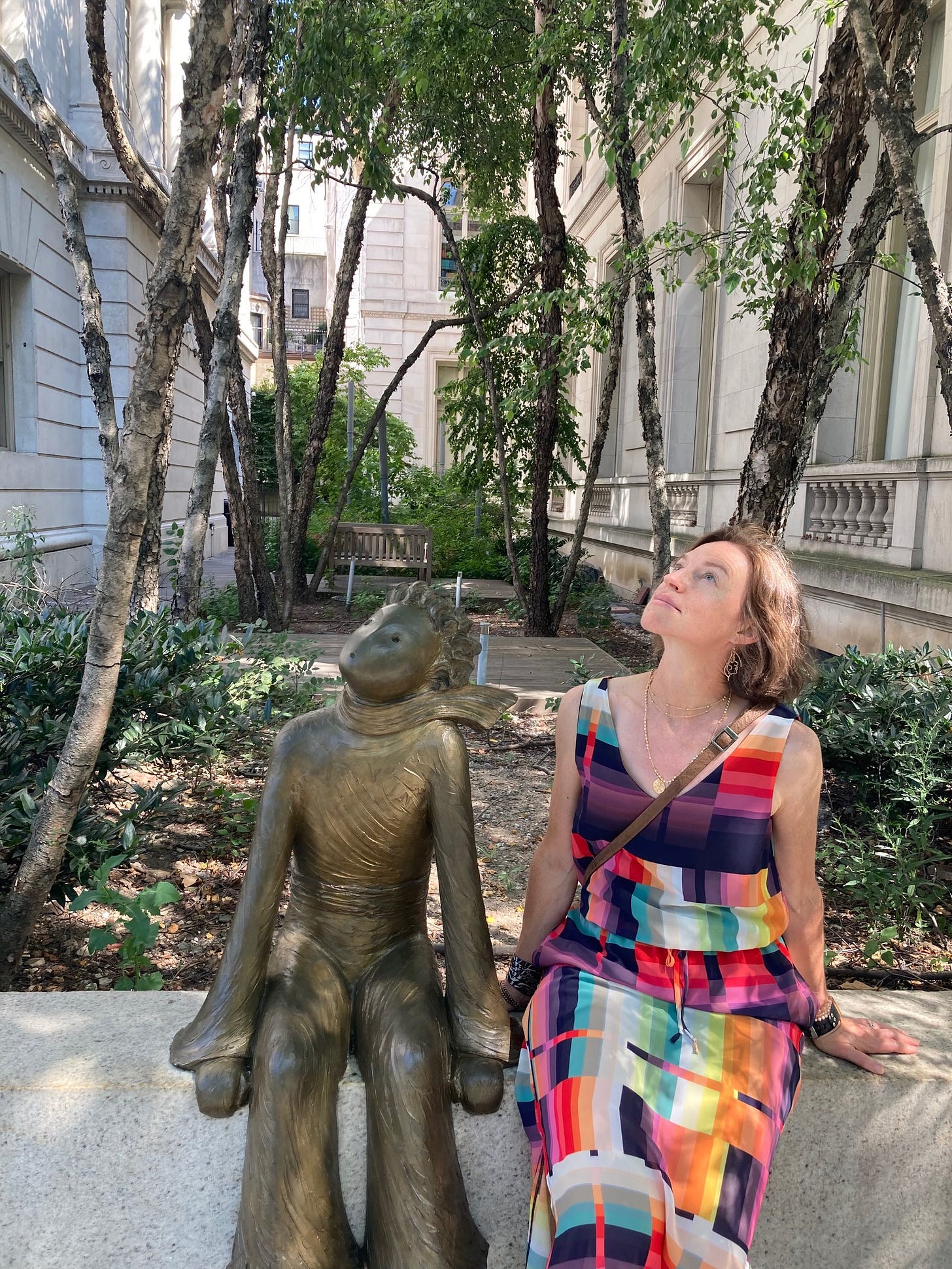 Christina Marlett, the author, sitting next to a bronze statue of the Little Prince. They are both looking skyward. 