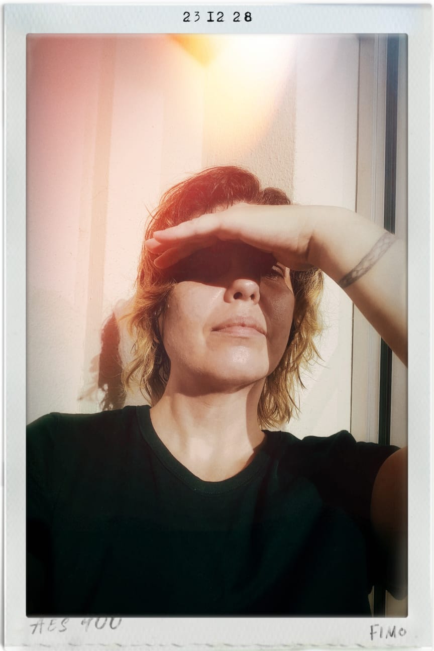 eu sentada com o sol batendo no rosto a mão levantada pra proteger meus olhos e com cabelos molhados