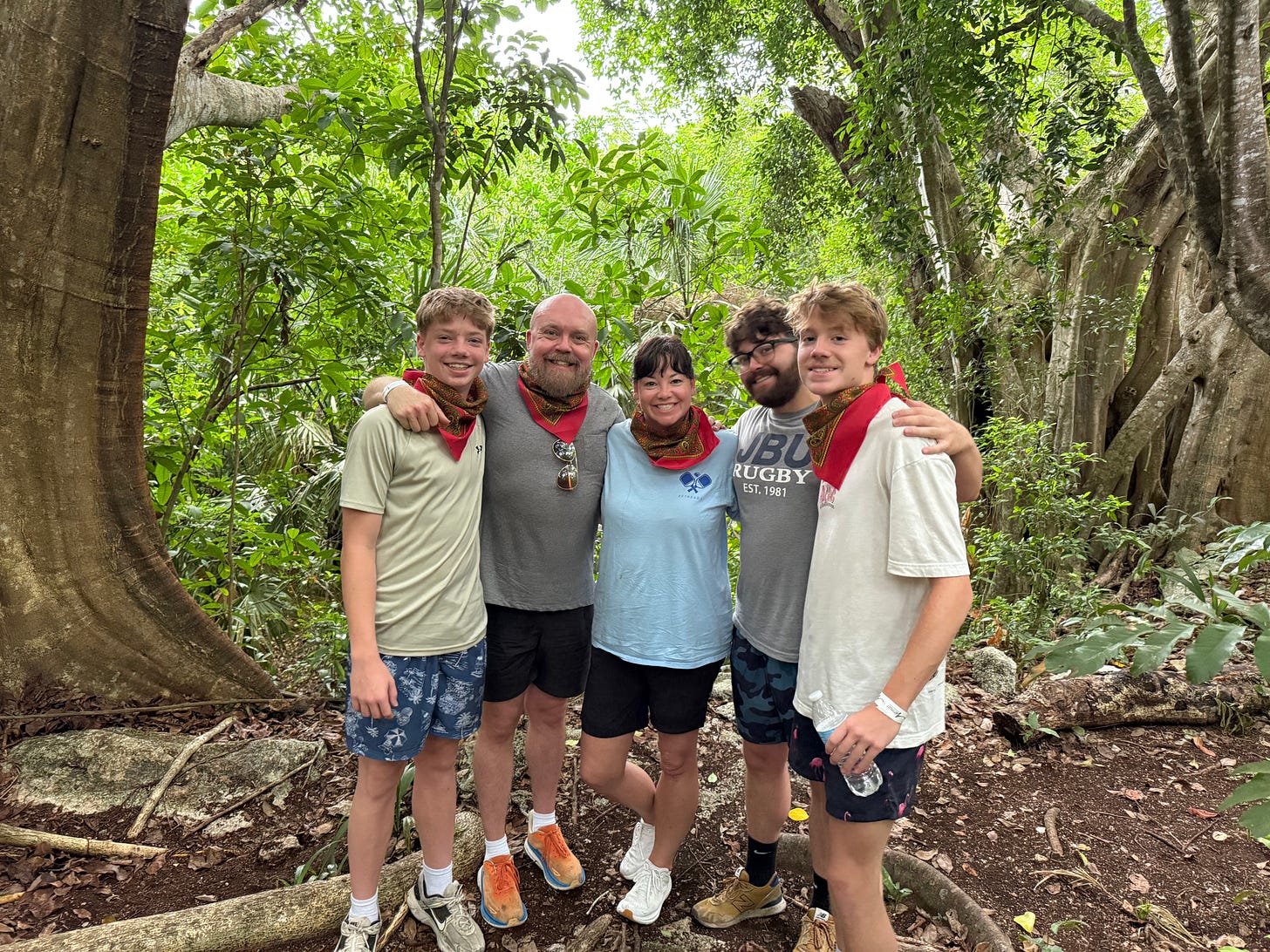 Daniel and Rhonda standing outdoors in a wooded setting with their three sons, all smiling with their arms around one another. Daniel and Rhonda standing outdoors in a wooded setting with their three sons, all smiling with their arms around one another.