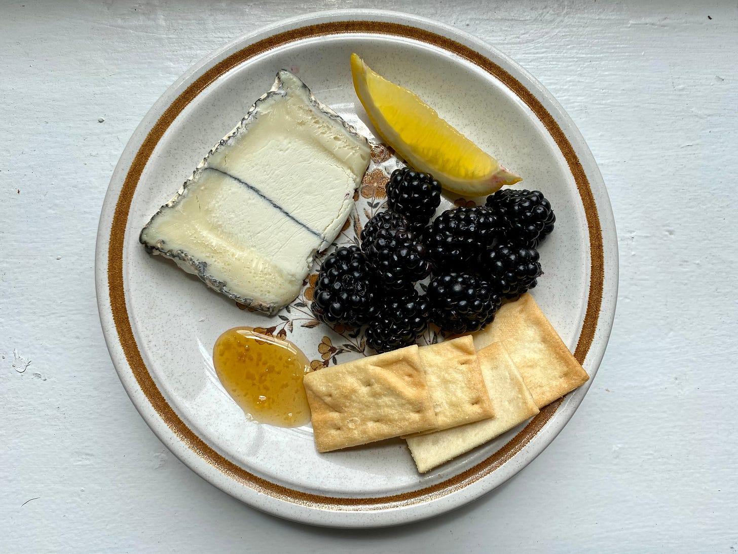 Humboldt Fog on a plate with a slice of lemon, blackberries, olive oil crackers, and splot of honey