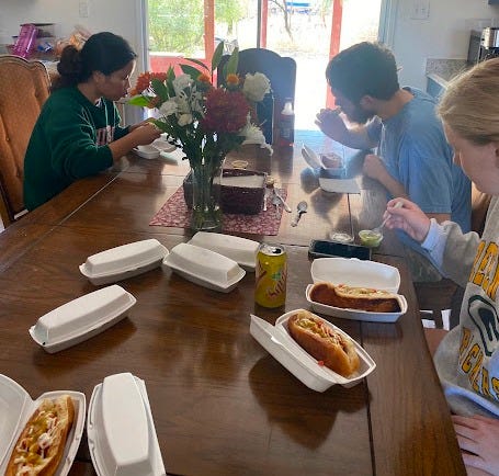 Three young adults sit around a table eating Sonoran dogs.