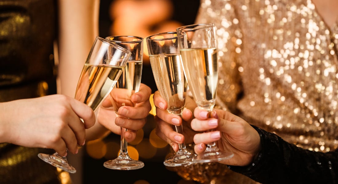 Four glasses with champagne being clinked together by people wearing gold dresses