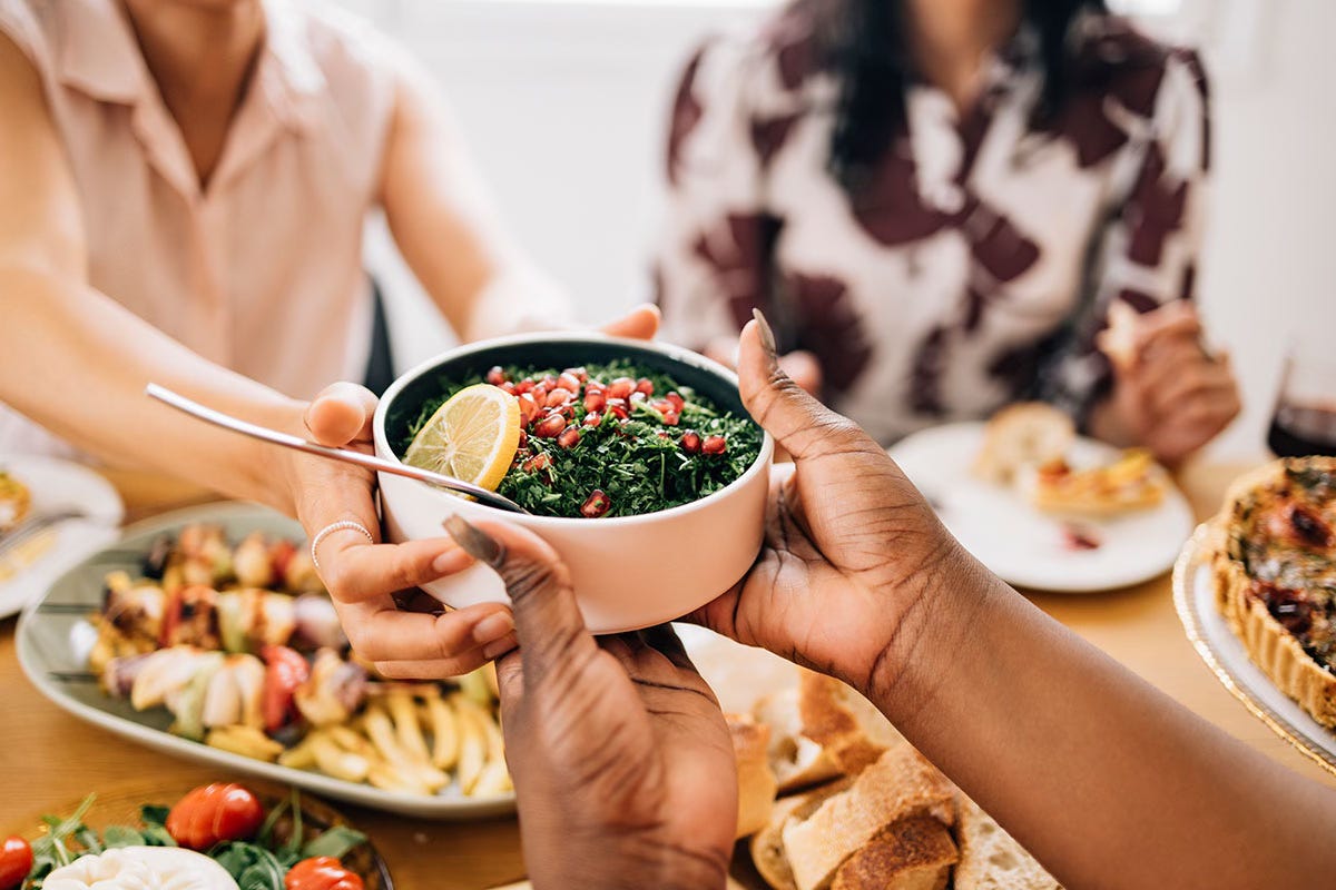 Close-up of women's hands passing a bowl of salad at a shared holiday meal, with blurred women in the background Close-up of women's hands passing a bowl of salad at a shared holiday meal, with blurred women in the background
