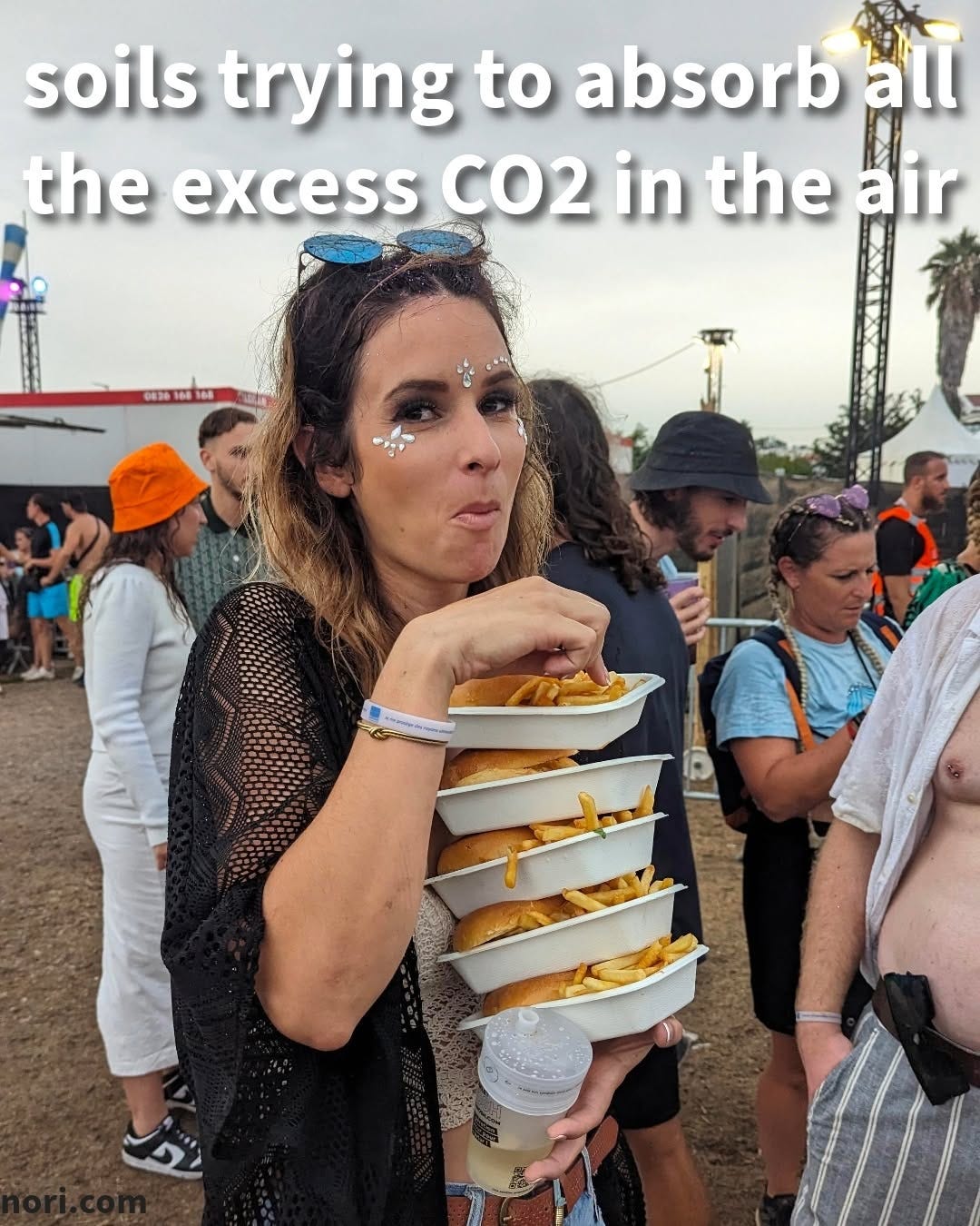 A woman at a music festival balancing a stack of six trays of fries while eating one, captioned "soils trying to absorb all the excess CO2 in the air".