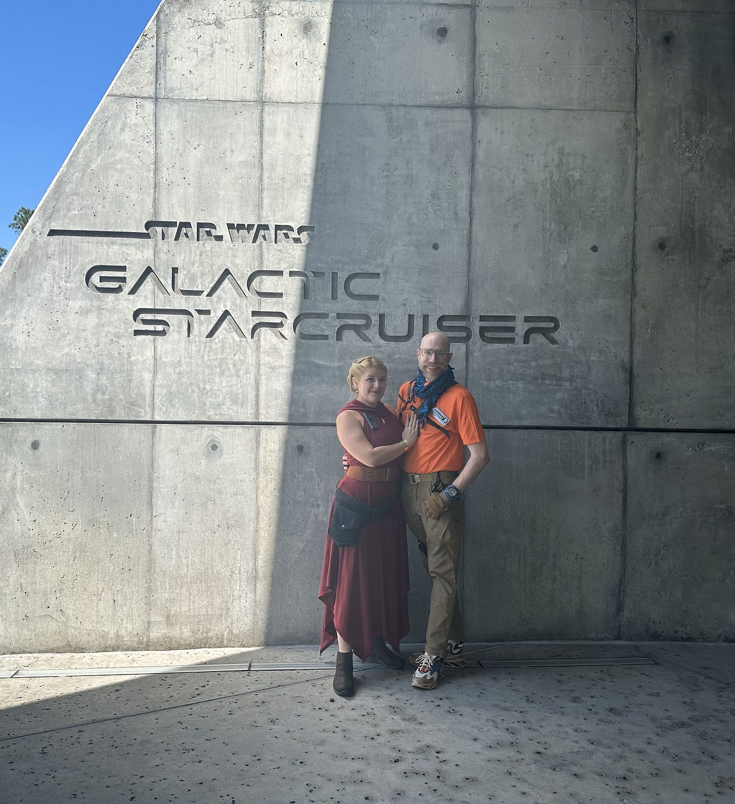 Cass and Noah, in their costumes, standing in front of the Star Wars Galactic Starcruiser concrete signage