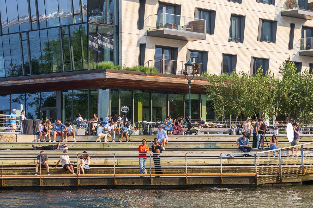 People sitting, walking, and filming on the steps of Pier 400 in Boston Harbor on a sunny afternoon