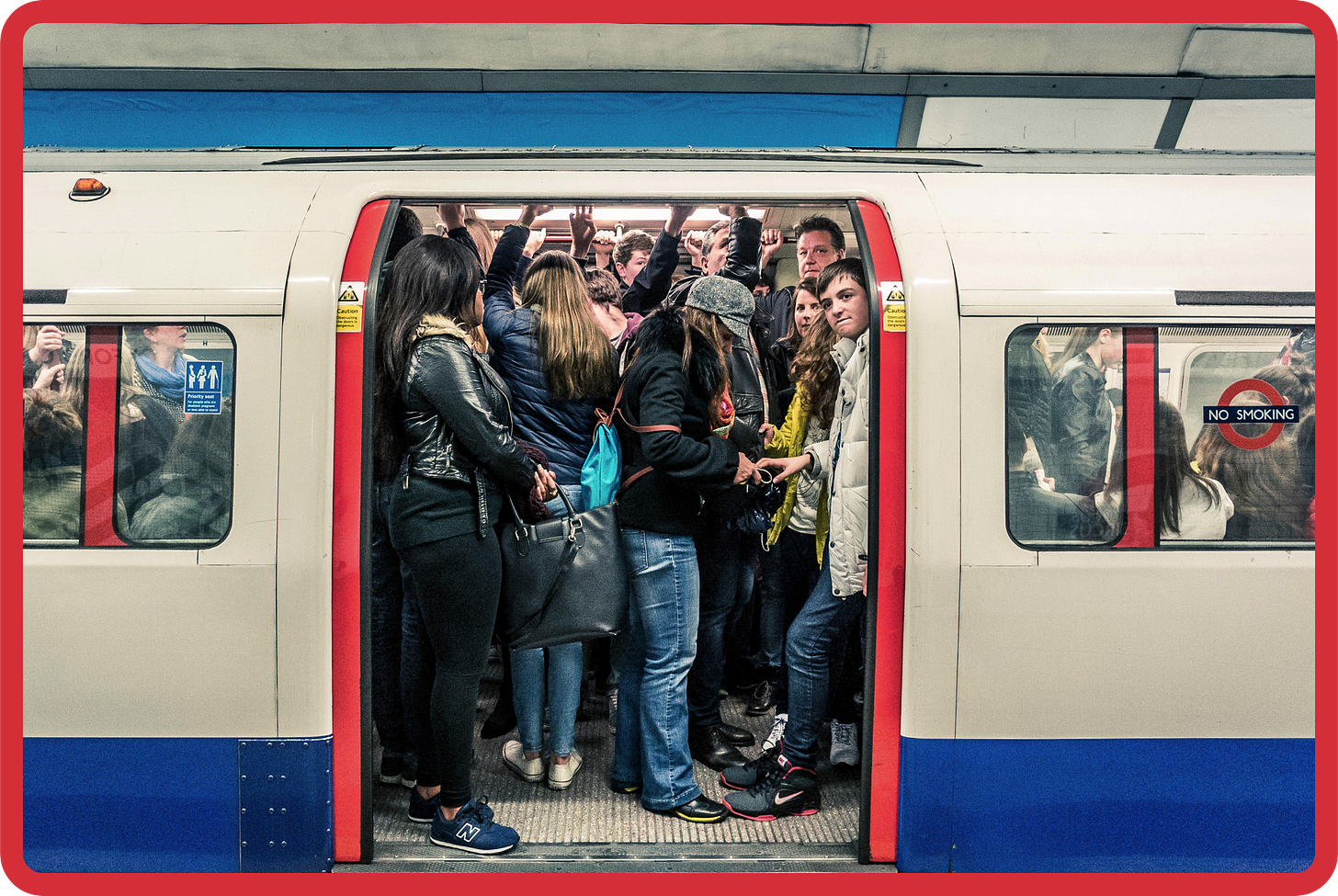 A photo of an extremely crowded Tube carriage. The doors are open and inside, people are standing, packed against one another, with their hands outstretched above their heads, holding onto the hand rails. A photo of an extremely crowded Tube carriage. The doors are open and inside, people are standing, packed against one another, with their hands outstretched above their heads, holding onto the hand rails.