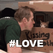 a man is kissing a kitten in a cardboard box that says kissing booth a man is kissing a kitten in a cardboard box that says kissing booth