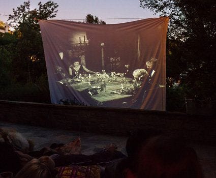 This may contain: people sitting on the ground in front of a projection screen at night, with one person watching