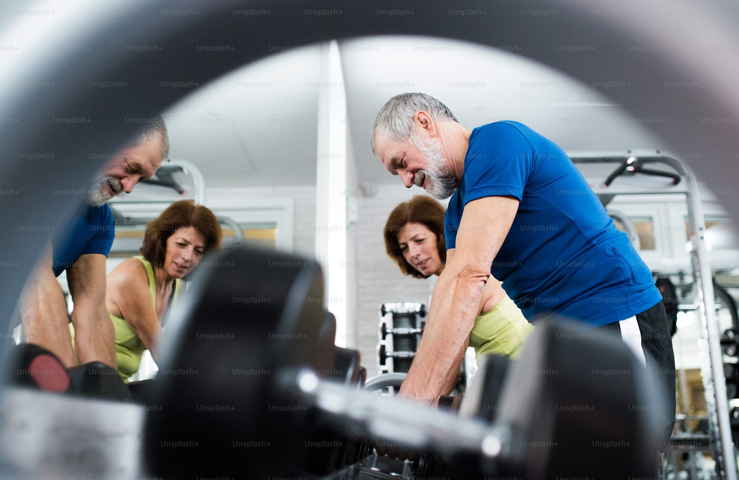 Beautiful fit senior couple in gym working out with weights
