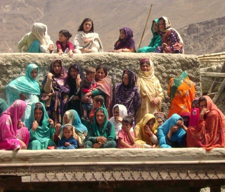 This may contain: a group of women sitting on top of a stone wall in front of some mountains