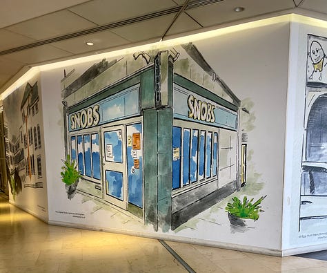 A mural showing a corner building in blue and green with the name 'SNOBS' written in white on its signage; a bright red and green and yellow archway with the words 'China Town Manchester' written on signage, with cars passing underneath; a mural showing a building with archways and 'MR EGG' signage in yellow, with a white car in front
