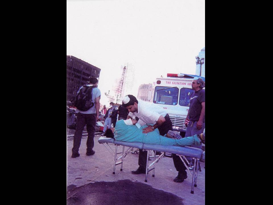 Chiropractor treats a person lying on a portable table in the street near a Salvation Army vehicle