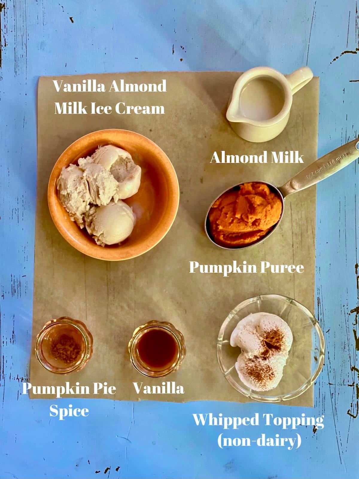 a blue table with ingredients, vanilla ice cream, pumpkin puree, almond milk, pumpkin pie spice, vanilla, with a text overlay saying those ingredient names.