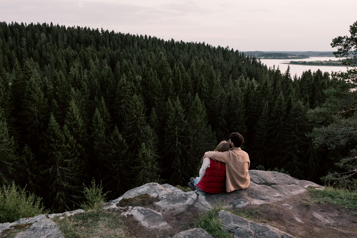 Ein Paar sitzt in der Natur auf einer Felskante mit Blick auf die Wälder.