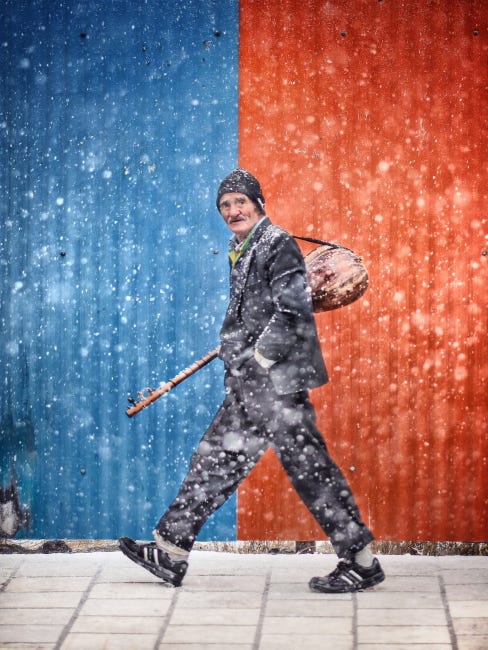 L'air âgé, vaguement inquiet, un musicien, reconnaissable à son lutte en bandoulière, traverse une rue enneigée