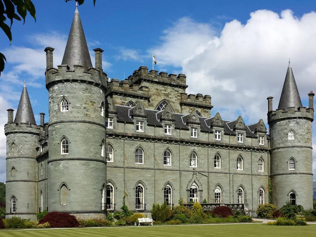 Inveraray Castle on our Loch Lomond and Inveraray Castle Tour dominates and fills this shot. A gothic revival castle built in the 1700's, it is grey, square and with four round corner towers with conical roofs. Green lawns are at the foot of the picture and a cloudy blue sky above. Inveraray Castle on our Loch Lomond and Inveraray Castle Tour dominates and fills this shot. A gothic revival castle built in the 1700's, it is grey, square and with four round corner towers with conical roofs. Green lawns are at the foot of the picture and a cloudy blue sky above.