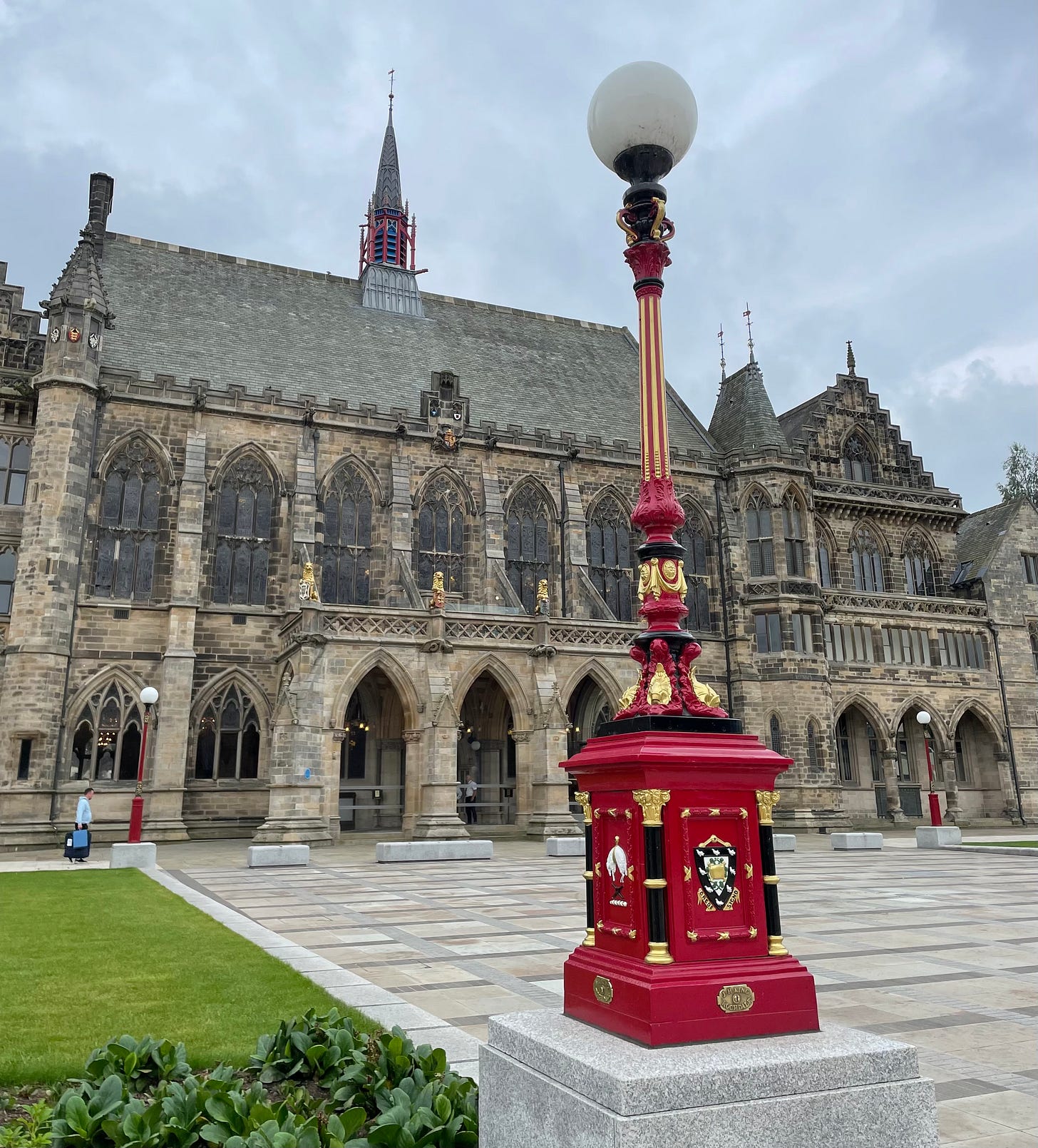 An ornate red and gold Victorian style lamppost in front of the Victorian Gothic splendour of Rochdale Town Hall. It's just stopped raining.