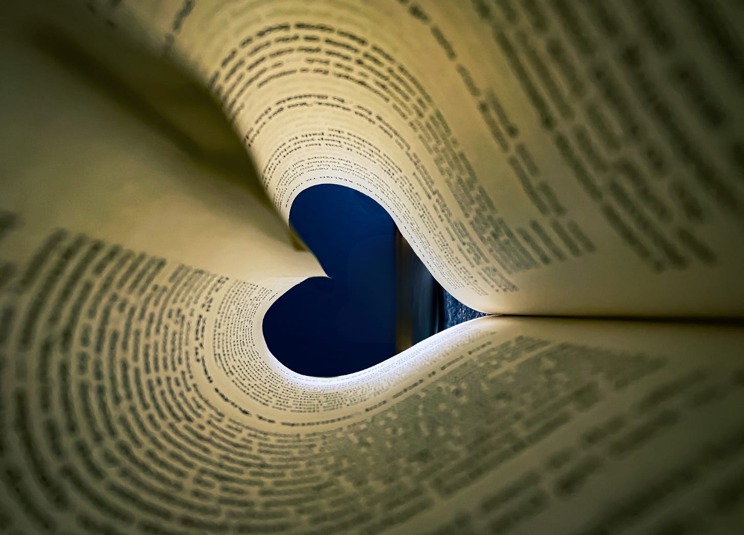 A close-up view through the rolled pages of a book, forming a tunnel with a heart-shaped opening at the far end. A visual metaphor for the inescapable pull of words and the love of writing.