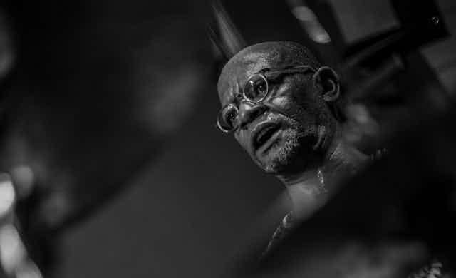 A black and white photo of an African man with a bald head wearing glasses, concentrating, his mouth open. A black and white photo of an African man with a bald head wearing glasses, concentrating, his mouth open.