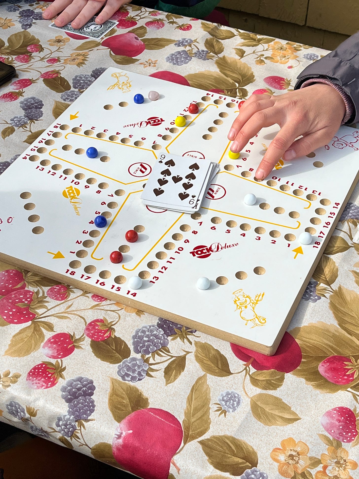 A wooden board game with marble pieces and a deck of cards. The name painted on the board is "tock deluxe" A wooden board game with marble pieces and a deck of cards. The name painted on the board is "tock deluxe"