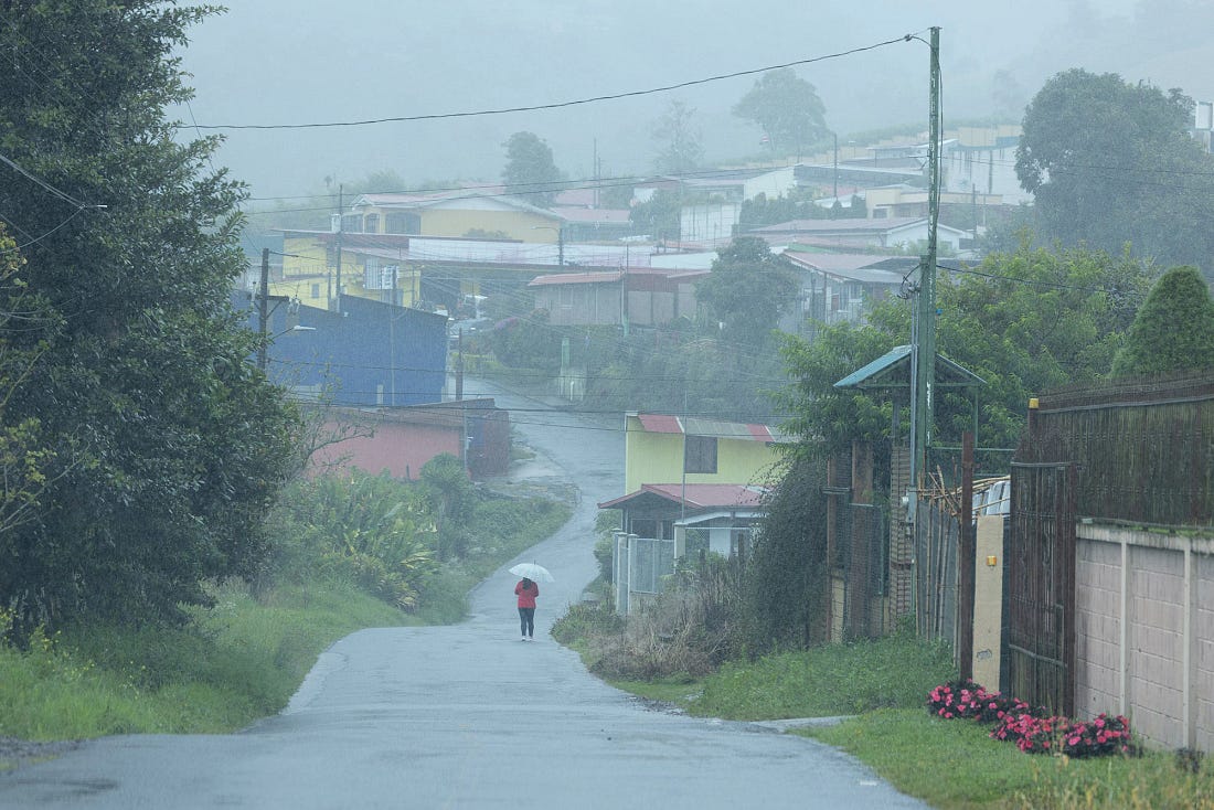 A misty street in a small town in Cartago Province, Costa Rica, with a lone person walking under an umbrella through light rain, houses and power lines fading into the fog. A misty street in a small town in Cartago Province, Costa Rica, with a lone person walking under an umbrella through light rain, houses and power lines fading into the fog.