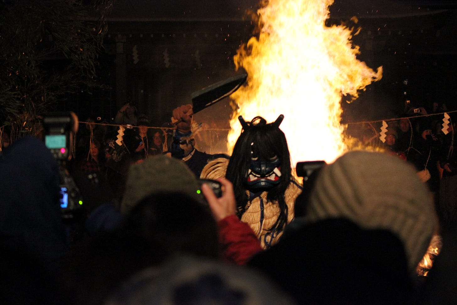 Blue faced demon wields cleaver in front of bon fire