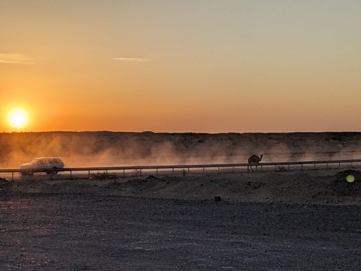 Sunset behind a dusty desert road with a 4x4 white car and camel. Sunset behind a dusty desert road with a 4x4 white car and camel.