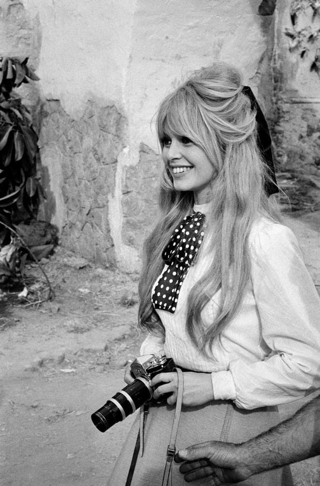 This may contain: a black and white photo of a woman with long hair holding a camera in her hand