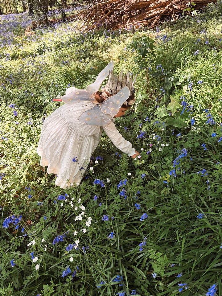Young girl picking flowers in a bluebell forest, and a boy helping her climb a log, both in costume