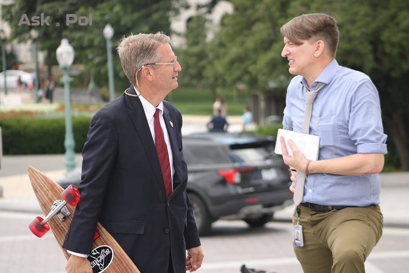 A man in a suit holds a wooden longboard while asnwering a reporter's questions. Photo: Logan Johnson for © www.askapol.com