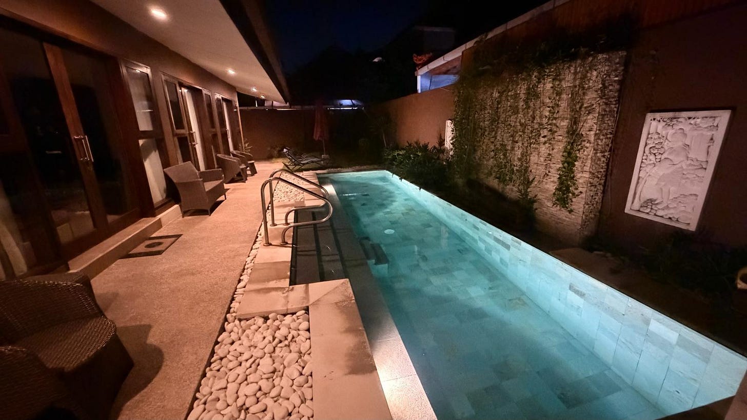 Nightime pool at a Bali villa beside a neighboring family compound.