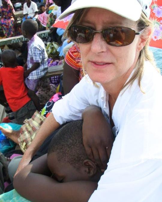The author holds a sleeping Tanzanian child against her chest on a crowded passenger boat. The author holds a sleeping Tanzanian child against her chest on a crowded passenger boat.