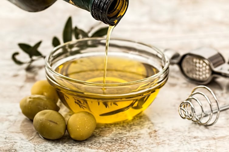 olive oil pouring into a glass dish, with some green olives olive oil pouring into a glass dish, with some green olives