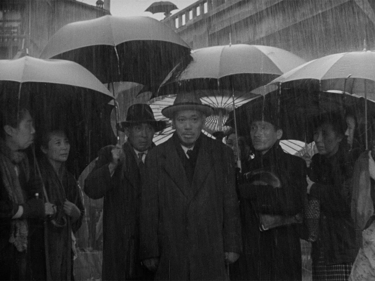 Ikiru | Still features Takashi Shimura as Kanji Watanabe surrounded by fellow bureaucrats in the rain.
