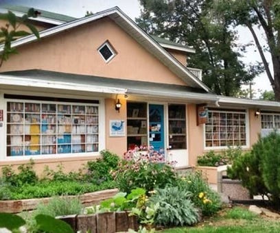 the store front for op. cit. books in Taos, with beige stucco, white wooden trim, and an abundance of flowers platned out front the store front for op. cit. books in Taos, with beige stucco, white wooden trim, and an abundance of flowers platned out front