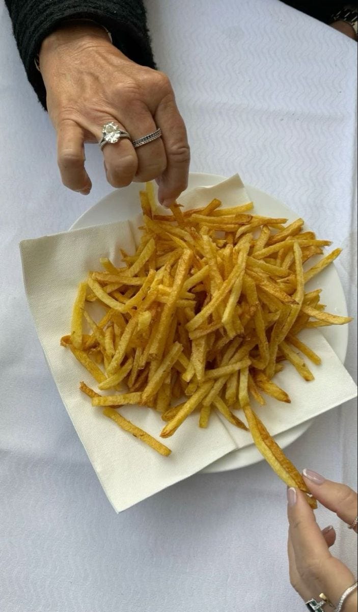 This may contain: two hands reaching for french fries on a plate