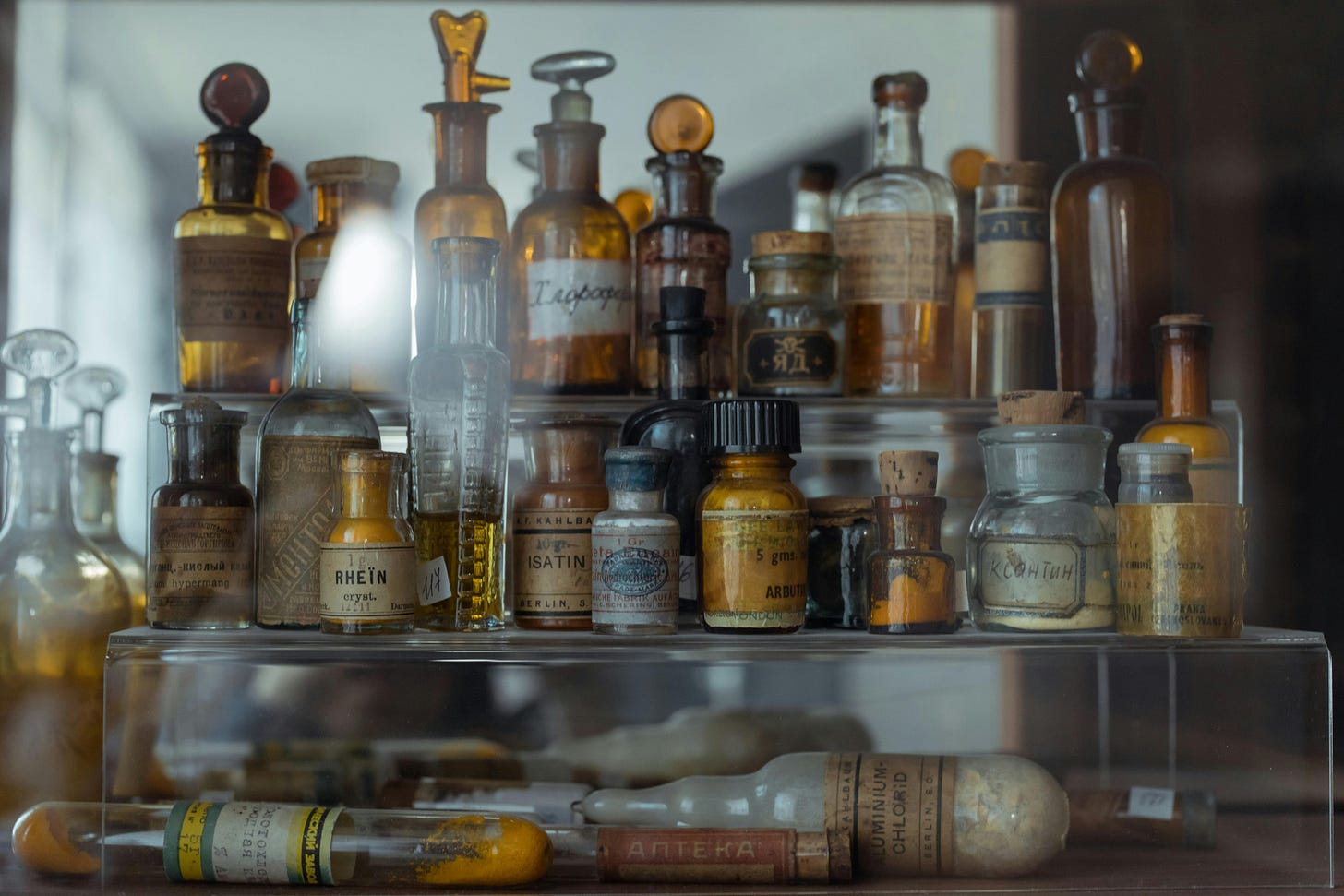 Three-tiered shelf full of glass apothecary bottles with old labels and writing on them.