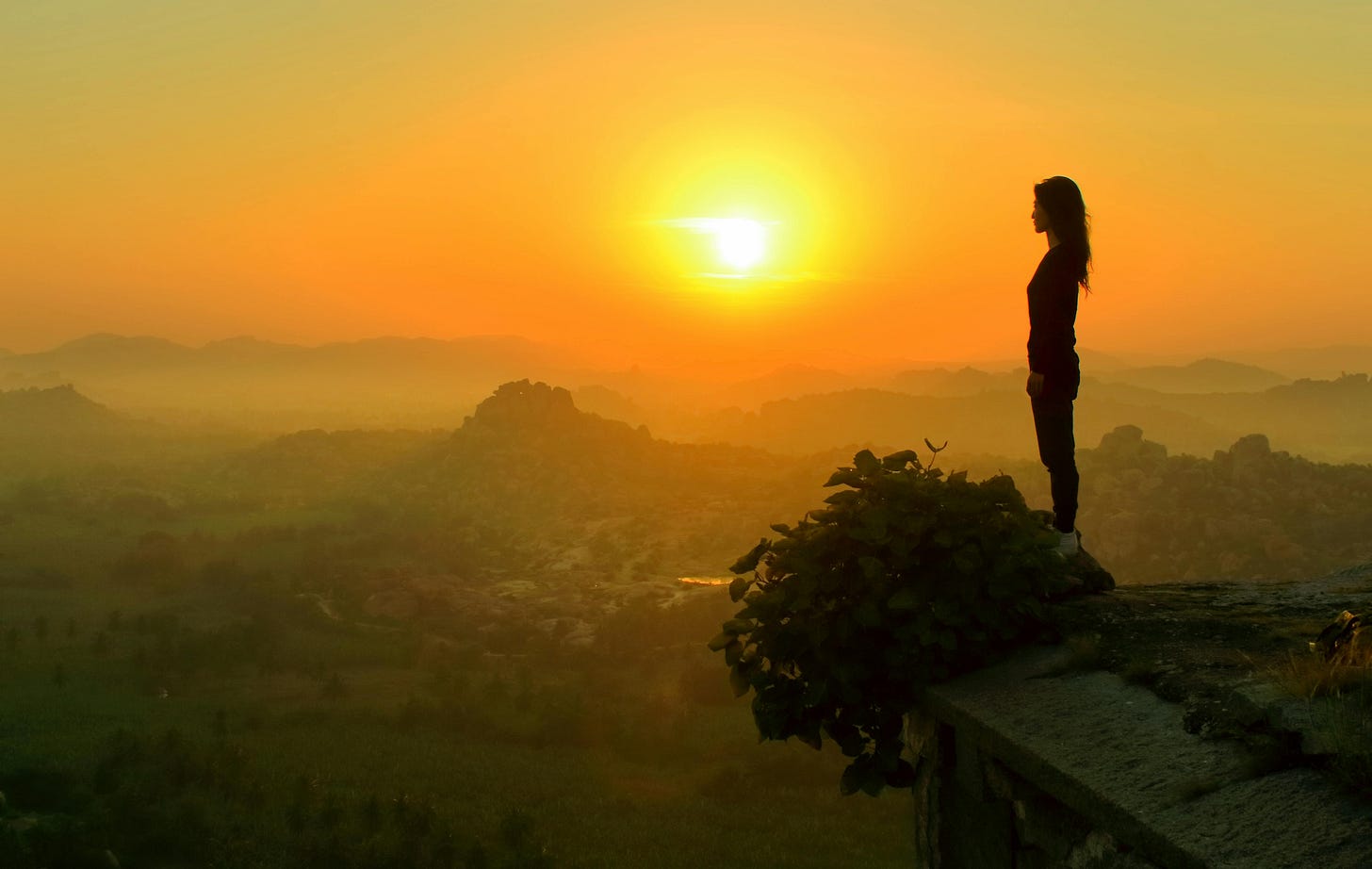 A woman standing on the edge of a hill in the sunset