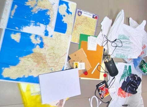 Dëshmia #1 – Paketime SIM: Kartela SIM dhe paketime aktivizimi të fotografuara si pjesë e inventarit, me kodet e sigurisë të redaktuara. | Dëshmia #2 – Harta dhe materiale të shtypura: Harta rajonale dhe dokumente letre të sekuestruara, që sugjerojnë planifikim lëvizjeje ose reference terreni. | Dëshmia #3 – Para dhe sende personale: Para të gatshme, dokumente dhe objekte personale të shtrira gjatë inventarizimit zyrtar. | Dëshmia #4 – Telefona dhe pajisje elektronike: Telefona të shumtë, karta memorie dhe pajisje të lidhura, të etiketuar si prova. | Dëshmia #5 – Mjete teknike dhe mjete ndihmëse: Kabllo, module elektronike dhe mjete të tjera ndihmëse, që tejkalojnë përdorimin bazik personal.